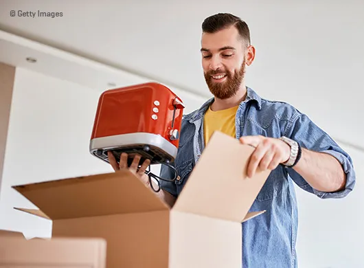 Un homme sort un grille-pain d'un carton de déménagement